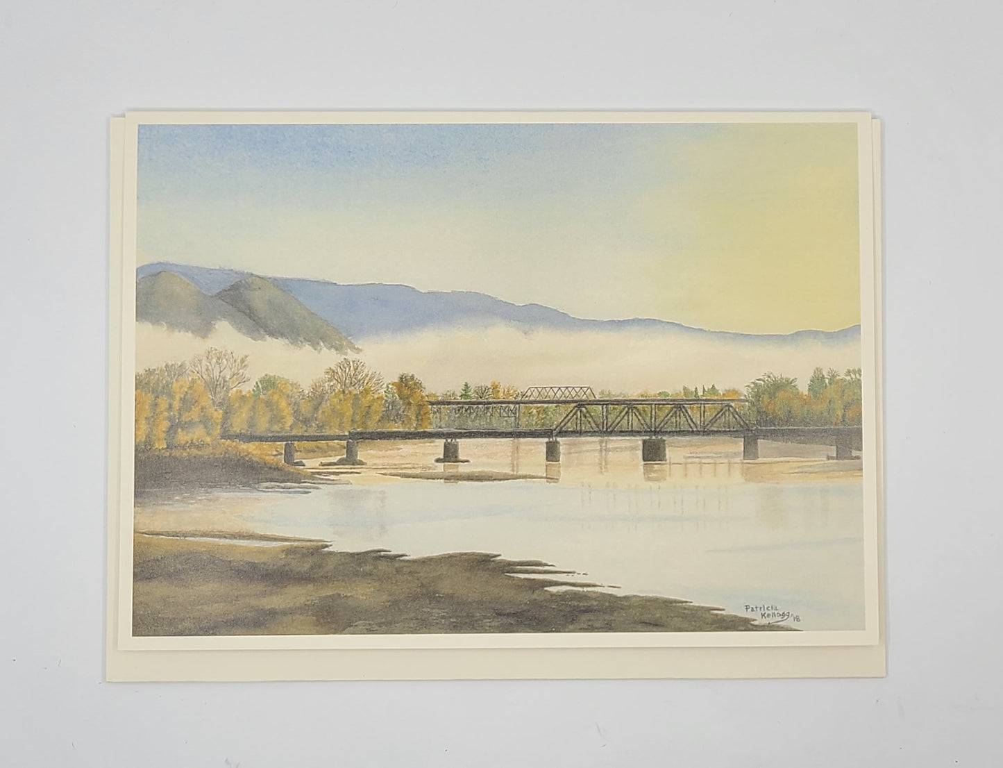 Watercolor painting of a bridge over a river with mountains in the background