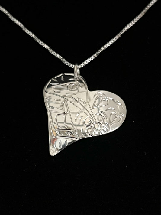 Silver heart-shaped pendant with humming bird design on a black background