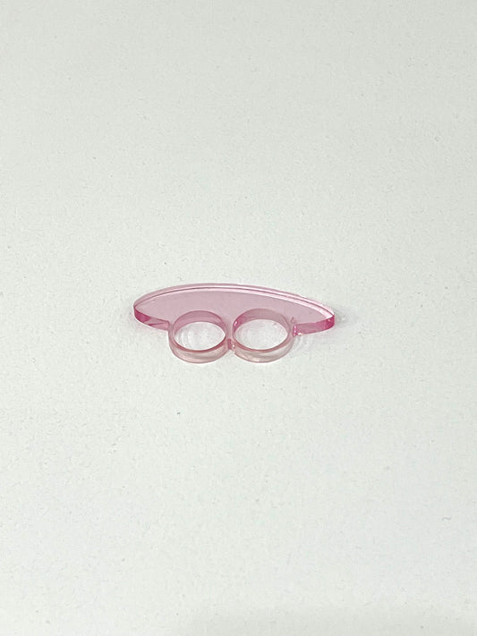 A pink acrylic double-finger ring with a curved, translucent design, placed on a plain white surface.
