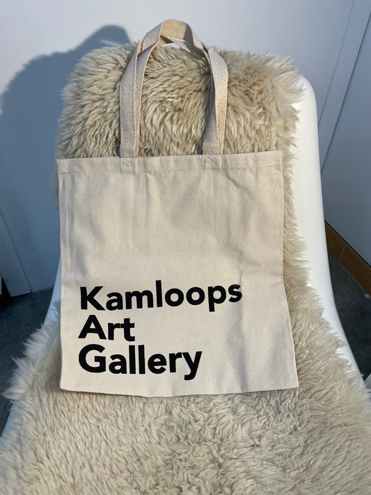 Tote bag with 'Kamloops Art Gallery' text on a fluffy white chair.