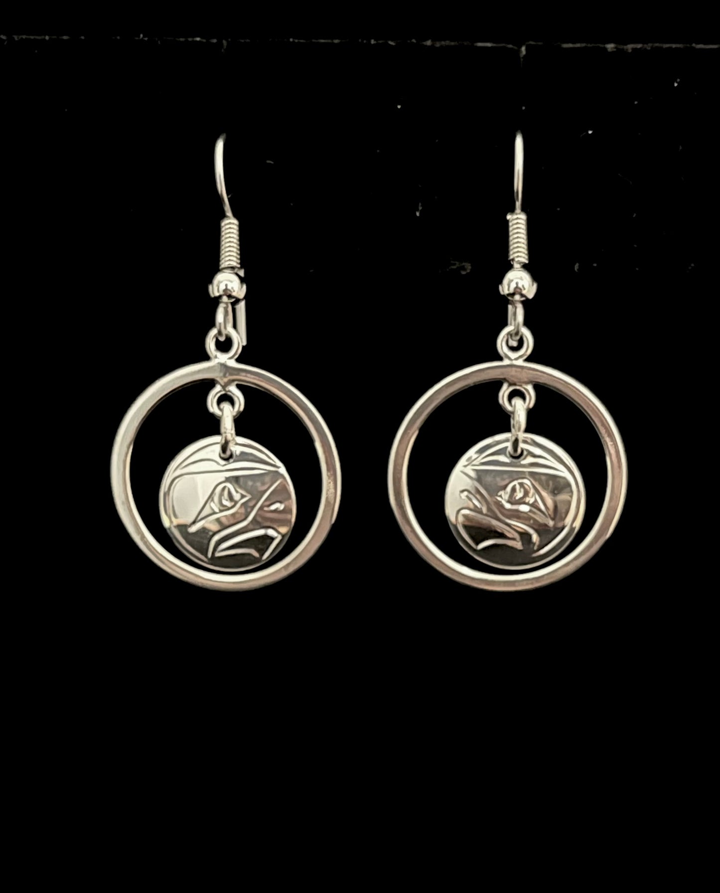 Silver hoop earrings with circular eagle designs on a black background