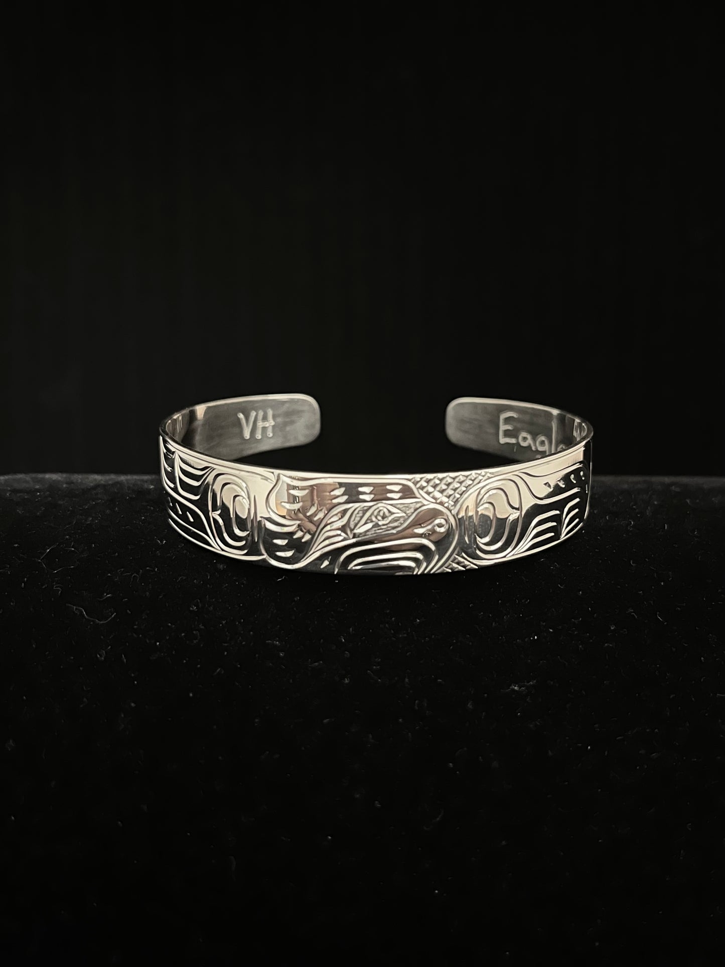 Silver bracelet with intricate eagle designs on a black background