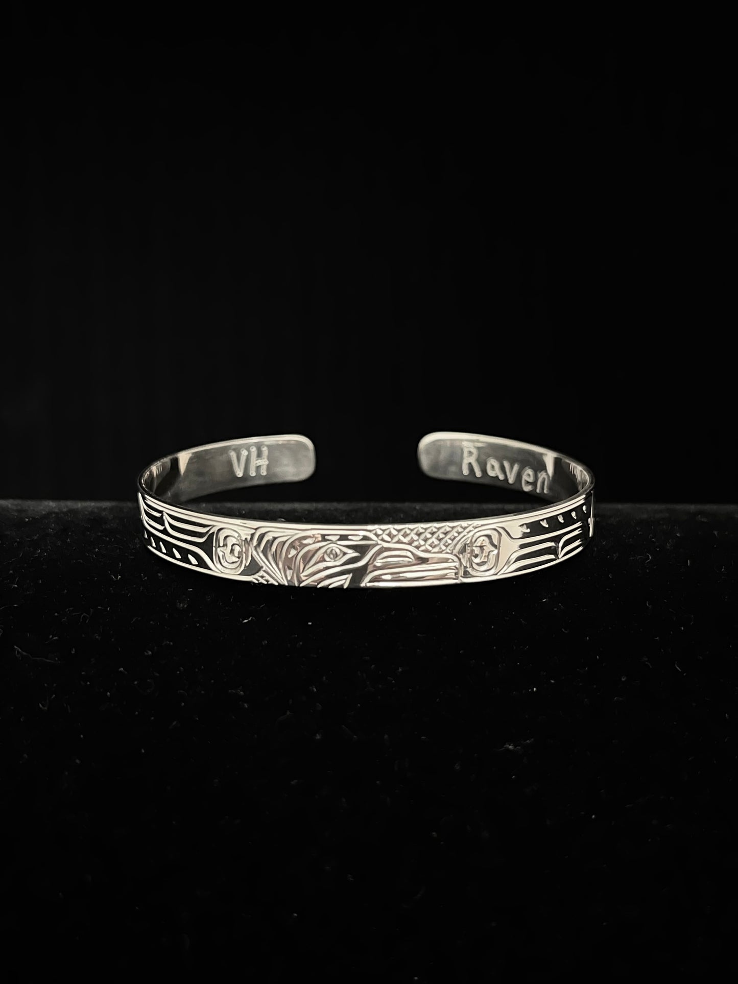 Silver bracelet with engraved raven design on a black background