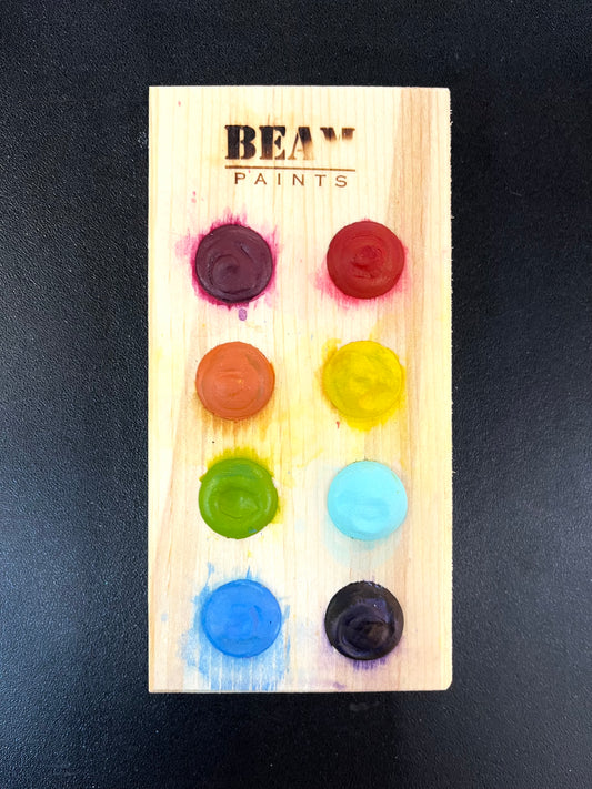 Set of colorful paint caps on a wooden board with 'BEAM Paints' branding.