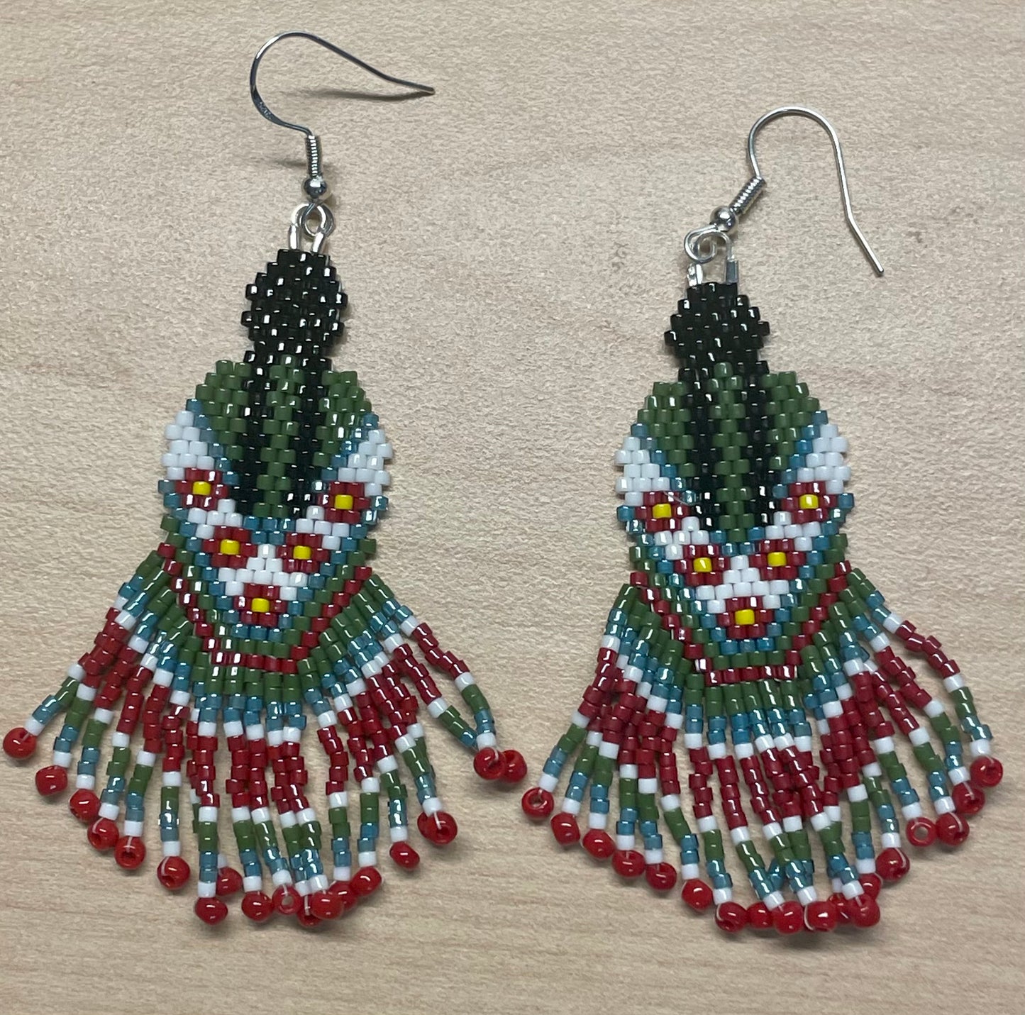 hand beaded earrings that represents and indigenous person with long breads wearing a green dress 