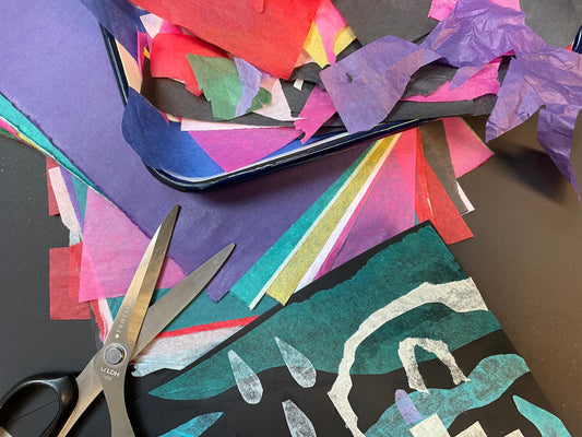 A rainbow of tissue paper colours are arranged on top of a background of black paper with a pair of open scissors in the lower left corner. 