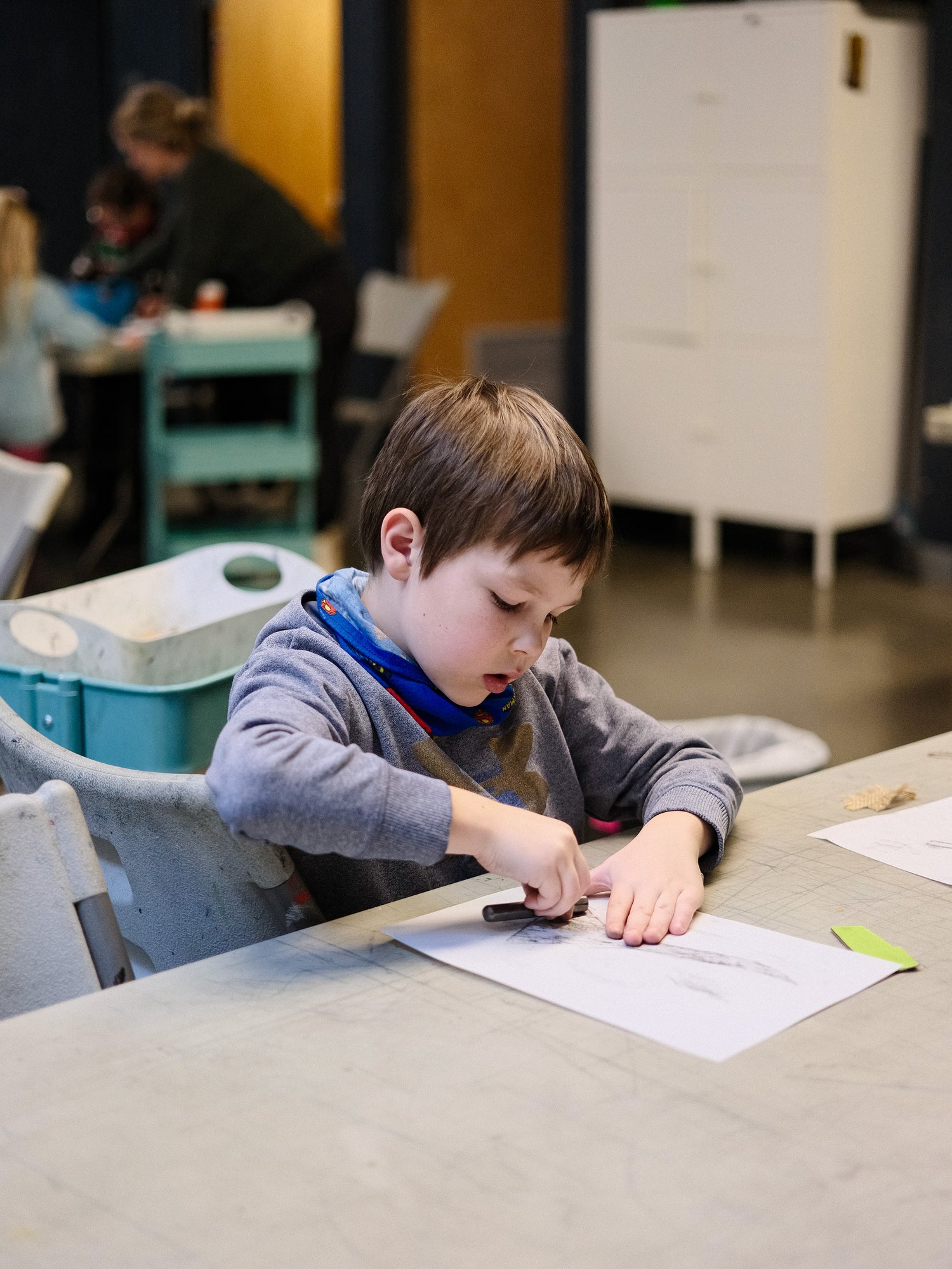 Child at a table with paper and crayon in an indoor setting