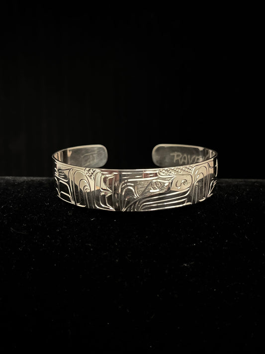 Silver bracelet with intricate raven designs on a black background