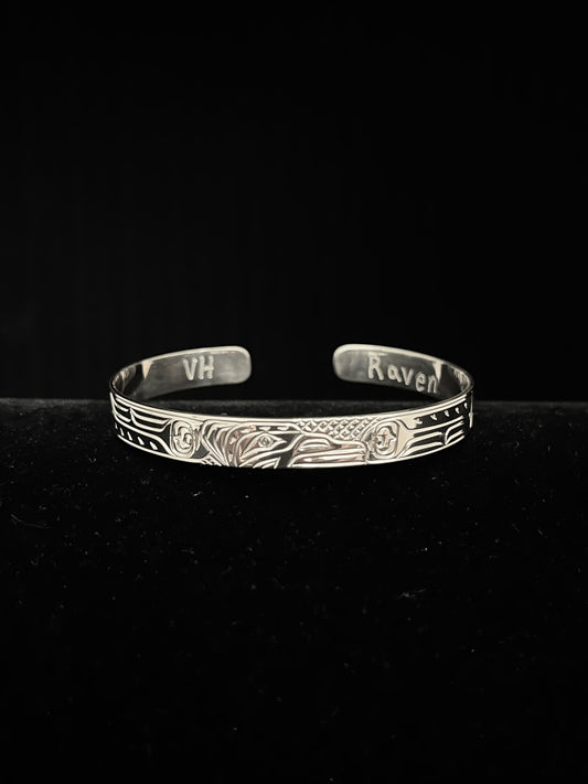 Silver bracelet with engraved raven design on a black background